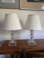 Pair of vintage square glass table lamps on wooden surface with beige fabric shades, unlit.