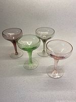 Four colored crystal stemmed and footed bowls arranged closely on a neutral surface, showing overall appearance and colors.