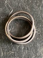 Close-up of the interlocked three silver bands of the rolling ring, showing surface texture and hallmark stamp.
