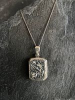 Close-up of the vintage sterling silver etched locket on chain against a dark background.