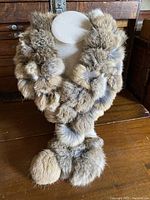 Front view of fluffy natural rabbit fur scarf on display stand showing the overall size and pom-pom ends.