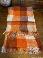Folded mohair throw displaying the fringe on both ends with visible check pattern colors on wooden surface.