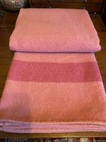 Folded wool blanket showing melon pink color with darker stripe and stitched edge detail.