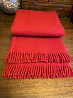 Folded crimson red wool blanket showing texture and fringe on wooden table.