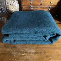 Folded double-sided wool fabric showing the teal blue/green side with nubbly texture on a wooden surface.