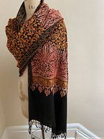 Black wool wrap with detailed tangerine, amber and melon embroidery draped on mannequin showing full length and pattern.