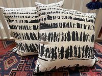 Two large linen pillows with cream base and hand printed abstract black linear patterns resting on a rug.