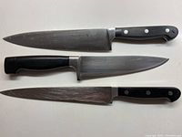 Three different Henckel brand kitchen cutting knives with black handles and stainless steel blades seen from top down.