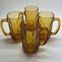 Four amber glass beer mugs grouped together. Side view showing the handled mugs with oval indentation pattern.
