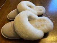 Side and angled view of cream suede slippers showing fluffy white sheepskin interior and folded cuff.