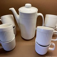 Full set photo showing white ribbed ceramic coffee/hot chocolate pot with lid and 8 matching mugs arranged around it