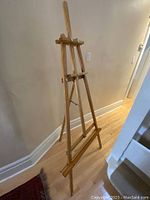 Full view of wooden tripod easel standing 68 inches tall against wall on hardwood floor.