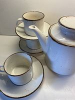 Teapot, cups stacked on saucers, showing cream ceramic with chocolate speckles and chocolate rim.