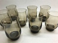 Top-down and angled view of 8 smokey grey glass tumblers grouped together showing uniform size and shape.
