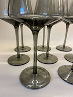 Close-up photo showing stems and bases of tall smokey grey wine glasses, emphasizing the translucent grey tint and rounded squared bowl shape.