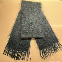Full view of the dark teal blue fringed scarf, showing its texture and length folded, lying flat.