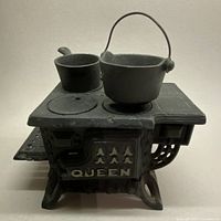 Front angle view of miniature cast iron 'QUEEN' stove with two miniature pots on top