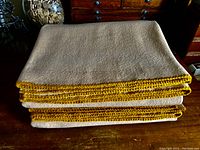 Stacked view of two folded merino wool blankets showing caramel color and hand crocheted blanket stitch edges in a darker caramel tone.