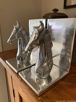 Pair of metal horse head bookends with right angle bases, showing the profile and reflective surfaces.
