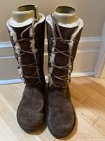 Front view of the pair of brown suede knee-high sheepskin lined boots with leather laces.