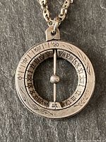 Front view of atlas sundial pendant showing Roman numerals and degree markings on circular rings with central ball and peg on post.