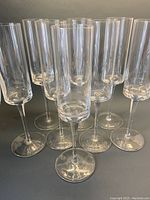 Group of 8 tall clear crystal champagne flutes arranged tightly on a dark surface, showing overall shape and quantity.