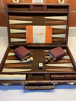 Opened backgammon case showing playing surface, dice cups, dice, doubling cube, and instruction booklet titled 'Backgammon Rules'.