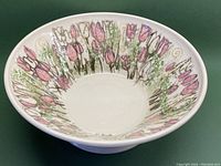 Angled side view of the bowl showing hand painted pink tulips and green foliage inside the bowl.