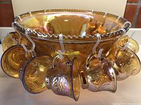 View of the iridescent amber punch bowl with 6 hanging cups visible, showing the scalloped edges and grapevine embossing on the glass.