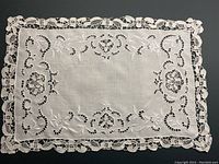 Full view of one white linen place mat showing intricate cutwork embroidery and scalloped lace edge, perfectly laying flat on a dark background.