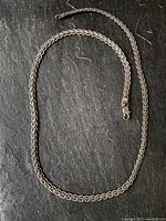 Full view of the entire sterling silver braided necklace laid out on a dark surface to show length and design.