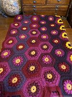 Top view of the blanket laid out showing hexagonal flower motifs in burgundy, purple, grey, and amber yarns.