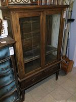 Full front view of antique solid oak china cabinet showing glass doors, drawer section, and legs