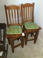 Pair of solid pine wooden swivel bar stools with slatted backs and green bee-patterned seat cushions, positioned side by side.