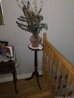 Full view of the wooden plant stand holding the ceramic vase with faux flowers on top.