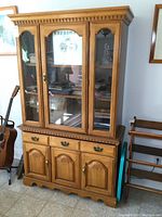 Front view of buffet and hutch showing solid maple construction, glass doors on hutch with decorative arches, ornate hardware, and scalloped edge on base of buffet.