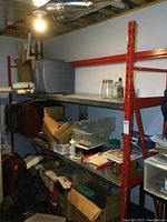Front view of red steel shelving frame with four galvanized shelves holding assorted boxes and items
