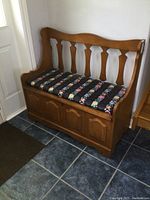 Front angle view of the wooden Lane deacons bench with floral cushion on seat, showing spindle-style backrest and storage compartment below.