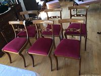 Full view of six vintage wooden dining chairs arranged on a wooden floor, five side chairs and one armchair.
