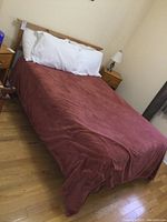 Full view of double bed with mattress and blanket covering it, pillows at headboard