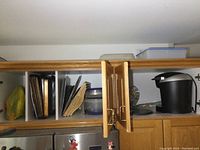 Upper cupboards opened showing various metal pans, wooden trays, plastic containers and a Keurig coffee maker with punch bowl set.