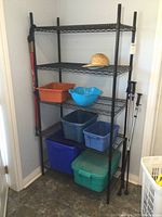 Full front view of the black metal shelving rack showing five shelves and some storage bins and outdoor gear beside it.