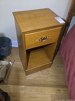 Front and angled views of the first solid wood night stand showing drawer with replaced decorative metal handle and open shelf below.
