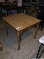 Photo showing full view of solid oak butcher block style table with visible marks, four rounded legs, placed on tiled floor.