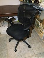 Full view of the black office chair showing mesh back, padded seat, and adjustable armrests on a five-wheel base.