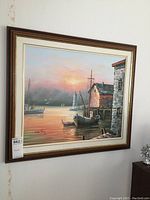 Framed oil painting depicting a harbor scene including a boat, lighthouse, and buildings at sunset, signed by the artist.
