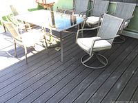 Full view of the patio set showing glass top table, 4 arm chairs and 2 swivel chairs with cushions, red umbrella and umbrella base visible.