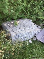 Stack of gray concrete pavers under foliage