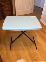 Full view of the portable collapsible table with blue plastic top and black metal frame on wooden floor.