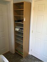 Front view showing full height wooden cabinet with 7 sloped perforated metal shelves and no door.